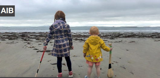 two children with their back to the camera looking out at the sea on a sandy beach