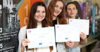 Photo of 3 female graduates from Ukraine holding up their certificates.